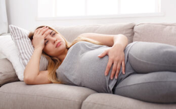 young pregnant woman holding her belly with one hand and her head with the other