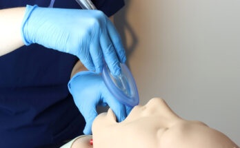 Laryngeal mask airway (LMA) Bering inserted in a simulated patient airway by a health care professional wearing gloves and surgical scrubs