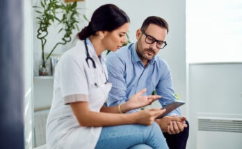 A healthcare professional discusses medical information with a patient in a clinical office setting, emphasizing cooperative understanding and technology use in the health field.