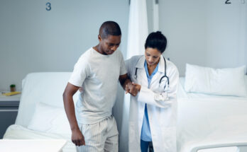Female doctor helping male patient to walk in the ward
