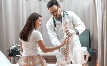 Female patient sitting with backs turned showing on spine model where she feel pain. Doctor holding spine model.
