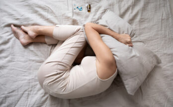 Depressed mature woman lying in bed with bottle of pills