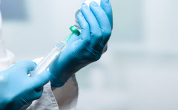 Hand mit Handschuhen zieht eine Spritze auf