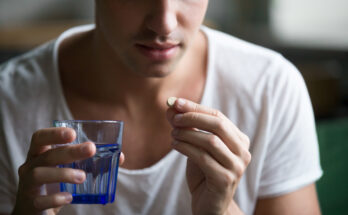 man holding glass of water taking pill, closeup