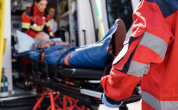Selective focus of paramedic in uniform carrying stretcher with patient in ambulance ca outdoors